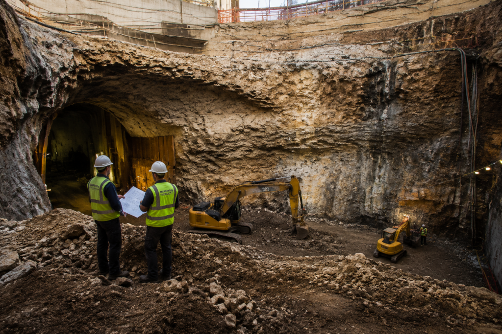 Underground construction excavation showing soil conditions, rock layers, and heavy equipment during site preparation